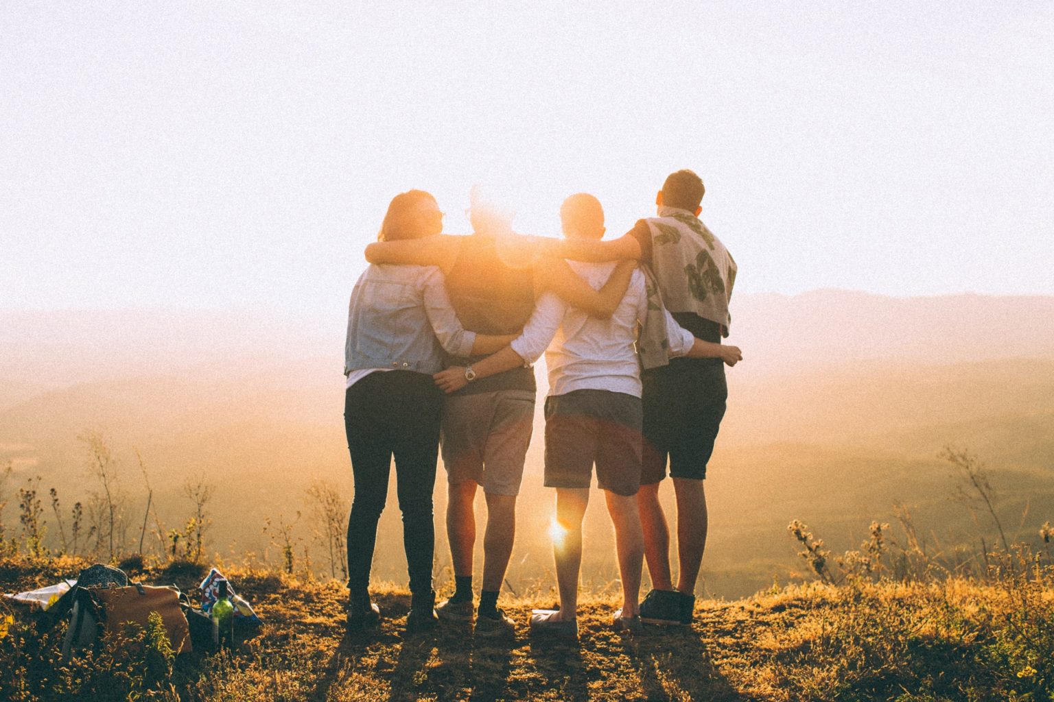 a group of people standing on a hill with the sun setting