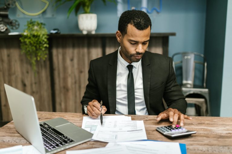 a man in a suit sitting at a table with a laptop and pen