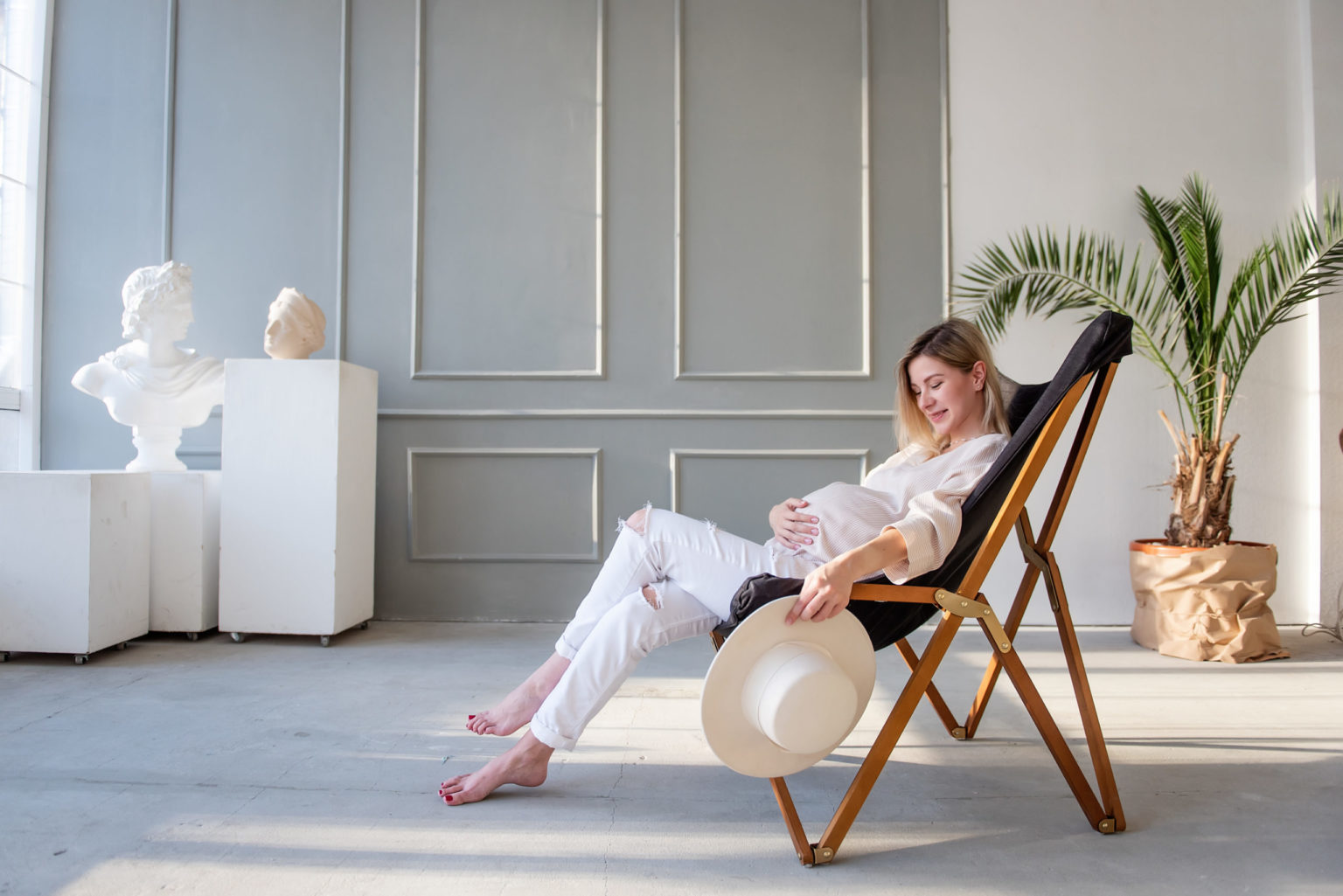 A young pregnant woman sits in a wooden deck chair, hugs belly. Happy motherhood, healthy pregnancy.