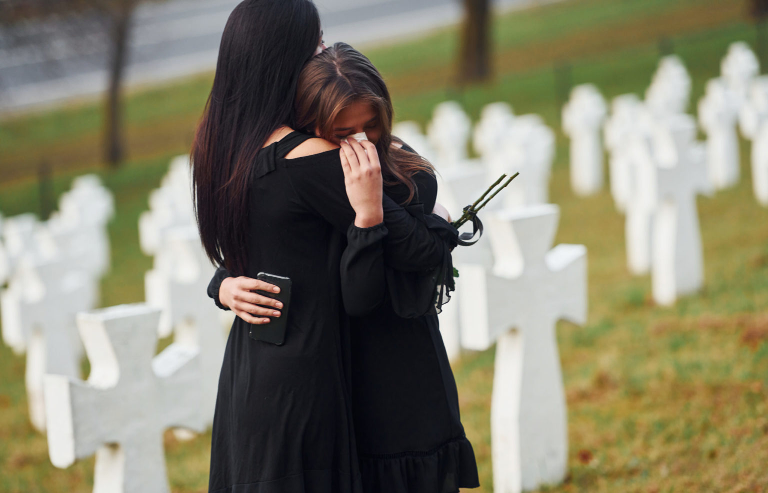 Two young women in black clothes visiting cemetery with many white crosses